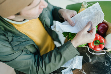 Urban shopper evaluating total cost of groceries, focusing on economic trends, mindful consumption,...