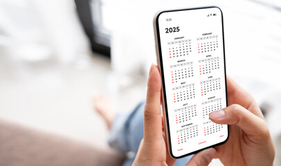 Businesswoman using smartphone with monthly calendar to plan 2025 activities. Scheduling and organizing plans. Technology and business concept.