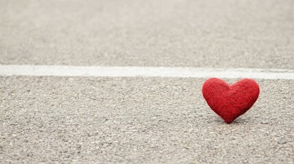 Fototapeta premium A red felt heart rests on a textured road beside a white line, symbolizing love and connection.