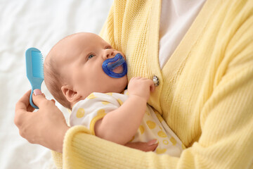 Mother combing her little baby's hair with cradle cap on bed, closeup