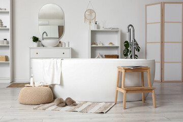 Soft slippers on rug near bathtub in stylish bathroom