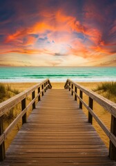 Obraz premium Wooden pathway to tranquil beach at sunset with vibrant sky and ocean view