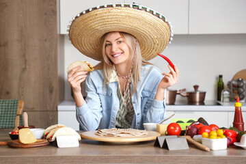 Young woman in sombrero hat with tasty taco and hot chili pepper at home