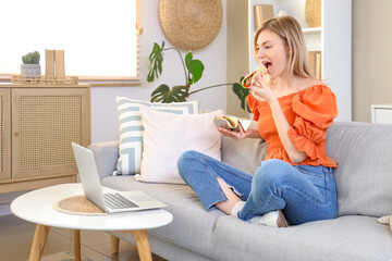 Young woman eating tasty taco on sofa while watching movie at home