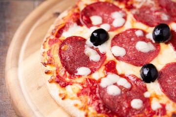 Pizza with salami and mozzarella cheese. Wooden background. Soft focus. Close up.
