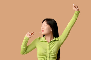 Pretty young Asian woman pulling chewing gum on beige background