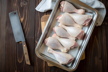 Fresh raw chicken legs placed on a baking tray with a knife, prepared for cooking.