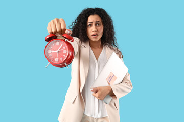 Stressed African-American businesswoman with laptop and alarm clock on blue background. Time...