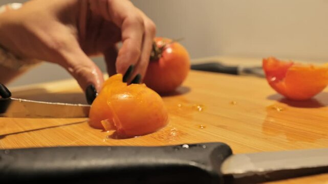 View of hands slicing tomato with knife during meal preparation on a wooden board