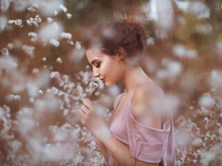 A young woman in a pink dress stands serenely among blooming white flowers, exuding elegance and...