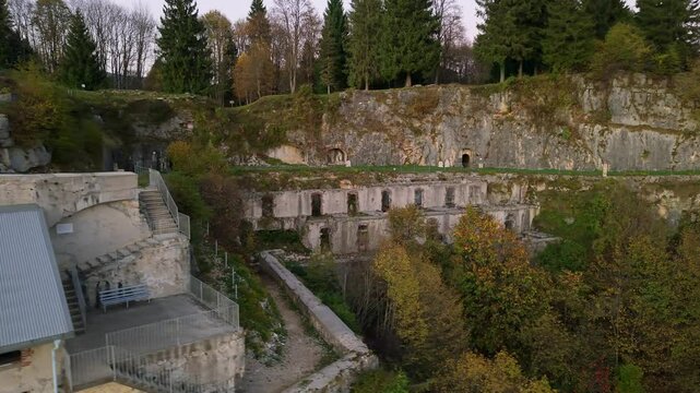 Aerial perspective of the Fort Punta Corbin, an Italian fortress located atop a rock spur, surrounded by lush trees and overlooking the tranquil Astico Valley.