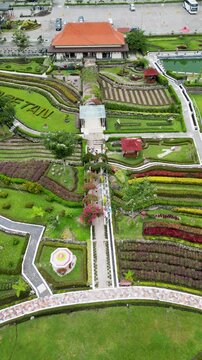 Refugia Garden in Magetan boasts vibrant flower beds in stunning patterns, surrounded by lush greenery and set against a serene, picturesque natural backdrop.
