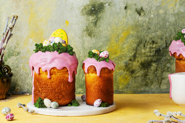 Easter cakes with pink icing decorated green sponge moss and colorful small eggs. Traditional Easter dish kulich. Food for catholic and Orthodox holiday. Yeast dough pastry. Colorful still life