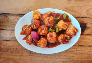 Chicken Chilly Momos in a spicy and flavorful sauce, served with colorful bell peppers and onions. Authentic Cuisine in Nepal momo over a rustic wooden background.