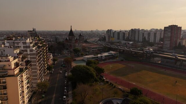 Aerial establishing shot of residential apartment at soccer field during sumset. Traffic on highway in Buenos Aires. Aerial wide shot. Parque Chacabuco in the evening. Capital of Argentina.