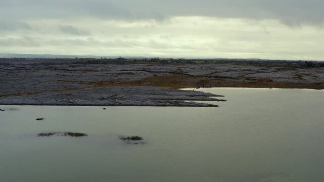 Aerial parallax shot of Burren landscape with seasonal lake in the foreground. Ireland.