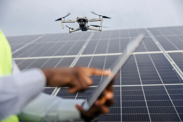 Selective focus on drone at solar farm with interracial engineer operating it with tablet in blurry...