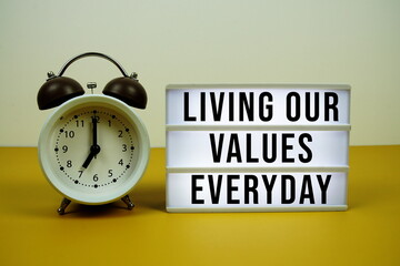 Living Our Values Everyday text on LED lightbox with alarm clock on yellow background