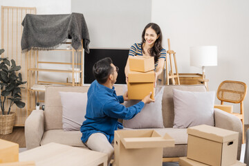Young couple sitting on a sofa, helping each other pack, collecting clothes, putting items in...