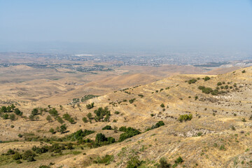 A desert landscape with a city in the distance. The sky is clear and the sun is shining