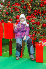Portrait of little toddler girl in hat, scarf and warm jacket in winter on decorated streets at...