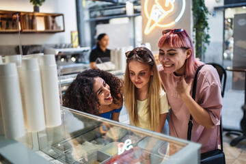 Three happy female friends choosing ice cream from a display in a parlor