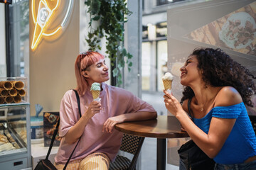 Two happy female friends enjoying ice cream cones at a cafe