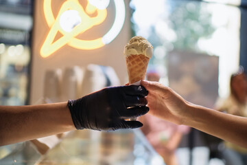Ice cream shop worker serving pistachio ice cream cone to customer