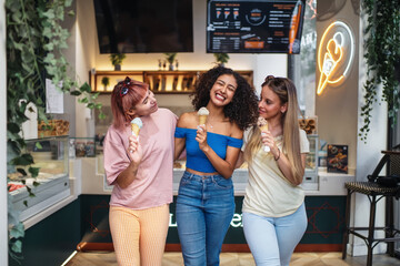 Three happy female friends enjoying ice cream cones in front of an ice cream shop