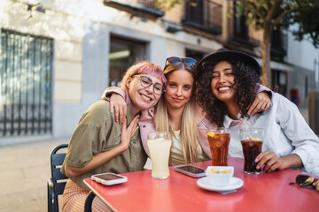 Three happy female friends embracing at outdoor cafe table