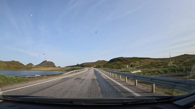 Driving through the tundra in northern Norway on E69 road. Surrounded by grassy hills with rocks and a scenic lake. A peaceful and remote landscape unfolds.