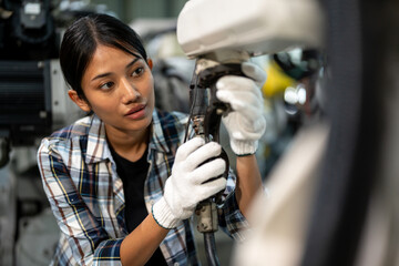 Focused female technician wearing gloves and plaid shirt carefully adjusting components of an industrial robotic arm inside a high-tech manufacturing facility.