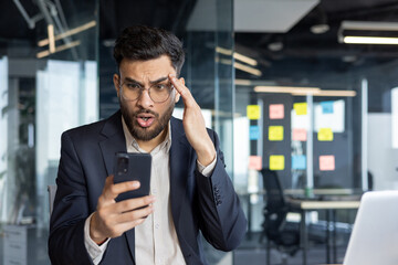 Man upset and disappointed holding phone in hands inside office. Businessman received online...