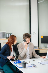 Fototapeta premium Two business workers talking on the smartphone and using laptop at office.