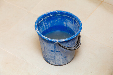 A blue bucket with water in it is sitting on a tile floor
