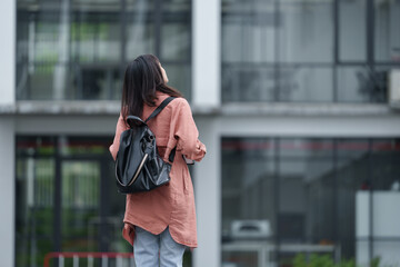 Young woman student with backpack looking up at university or college building contemplating future...
