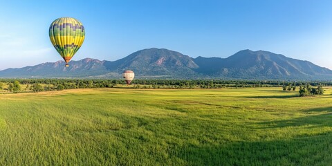 Obraz premium Hot Air Balloons Soaring Over Lush Green Fields and Majestic Mountains A Scenic Sunrise Adventure
