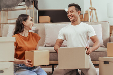 A happy young couple sits on a sofa, packing belongings into boxes, preparing to move to a new house, enjoying teamwork, organizing items, showing excitement, and embracing a fresh start
