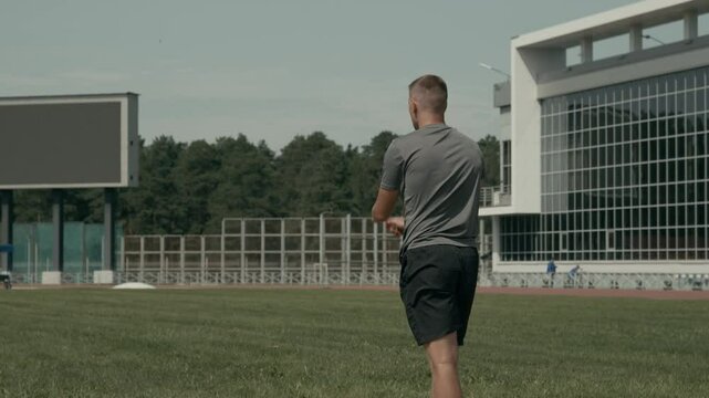 Medium full rear tilting shot of male track and field athlete with limb difference disability running on track, angling, throwing javelin onto green grass, while practicing for competition outdoors