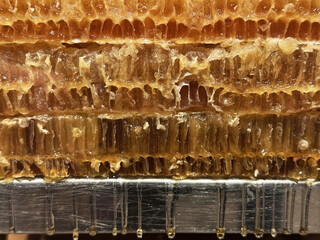 Close-up shot of a honeycomb filled with golden honey, dripping from the bottom onto a metallic...