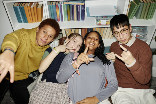 High angle view at of multiethnic group of teenage children posing together in library showing hand signs and smiling at camera, shot with flash - Powered by Adobe