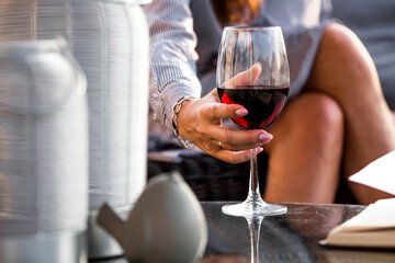 A glass of red alcoholic drink or wine in a woman's hand. A woman is resting on the veranda of a country house. The concept of relaxation, party or celebration.