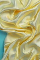 Soft, flowing yellow satin fabric draped elegantly, showcasing texture and shine against a teal backdrop.