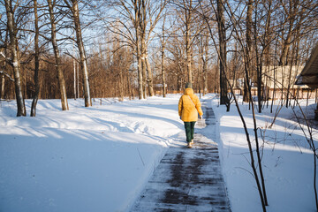 A person wearing a bright yellow jacket is leisurely walking down a snowy path surrounded by...