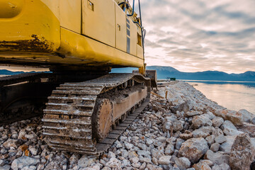 Side View of a Yellow Excavator on Rocky Terrain Near Water