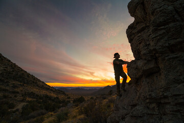 Silhouette of climber approaching rock climbing route at sunrise.