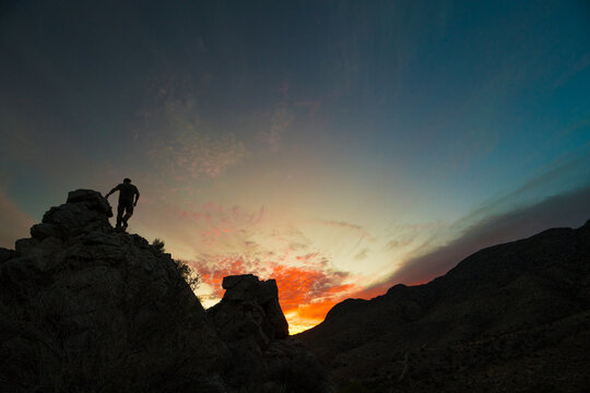 Silhouette of hiker standing on rocky mountain at sunrise.