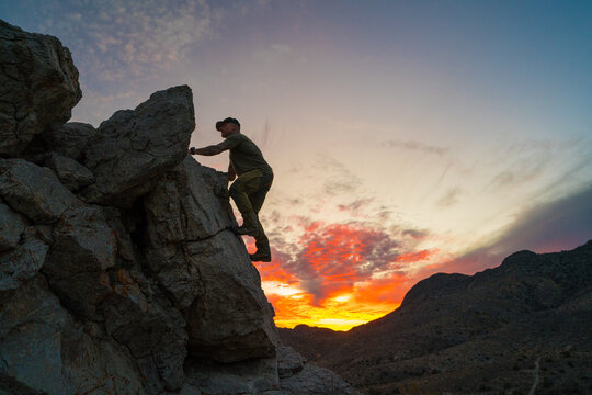 Side view of active person climbing over rocky terrain at daybreak
