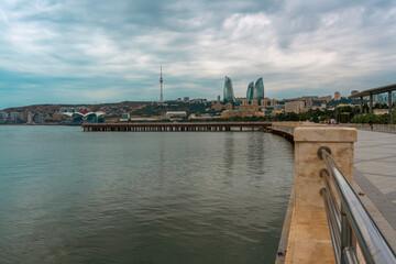 A city with a pier and a pier with a fence. The water is calm and the sky is cloudy