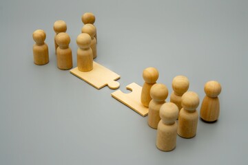 Two groups of wooden figures stand on opposite sides of a puzzle piece bridge. Mergers and...